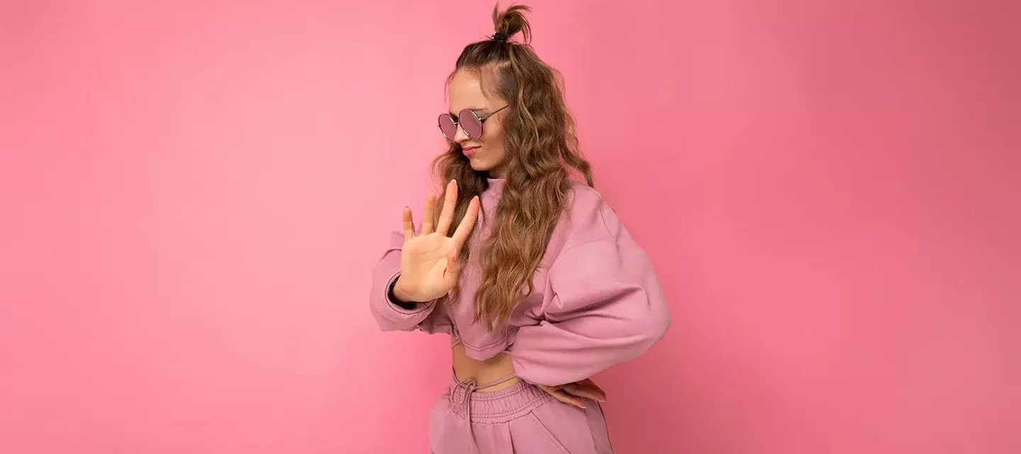 An attractive young woman on pink background with long hair in pink crop hoodie who has learned how to say no